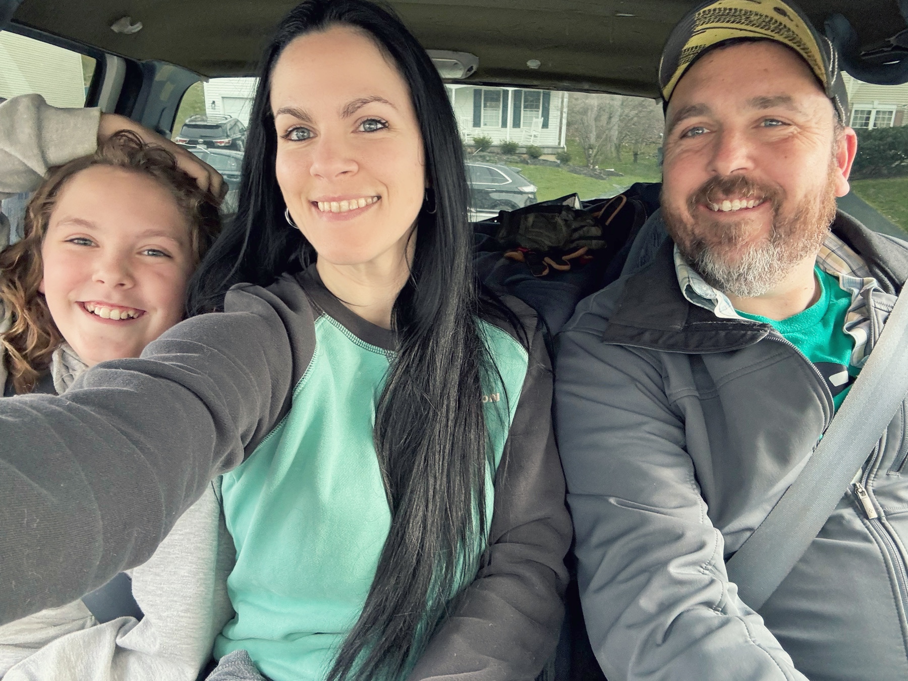 A family of three, young son, mother, father, sitting together in a car.