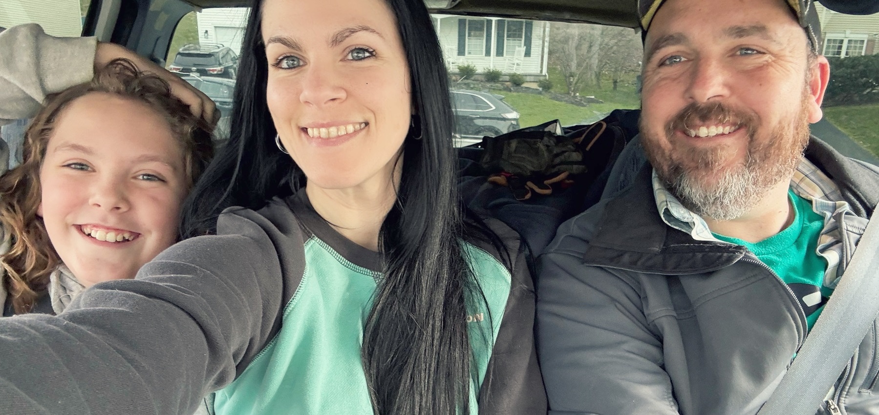 A family of three, young son, mother, father, sitting together in a car.